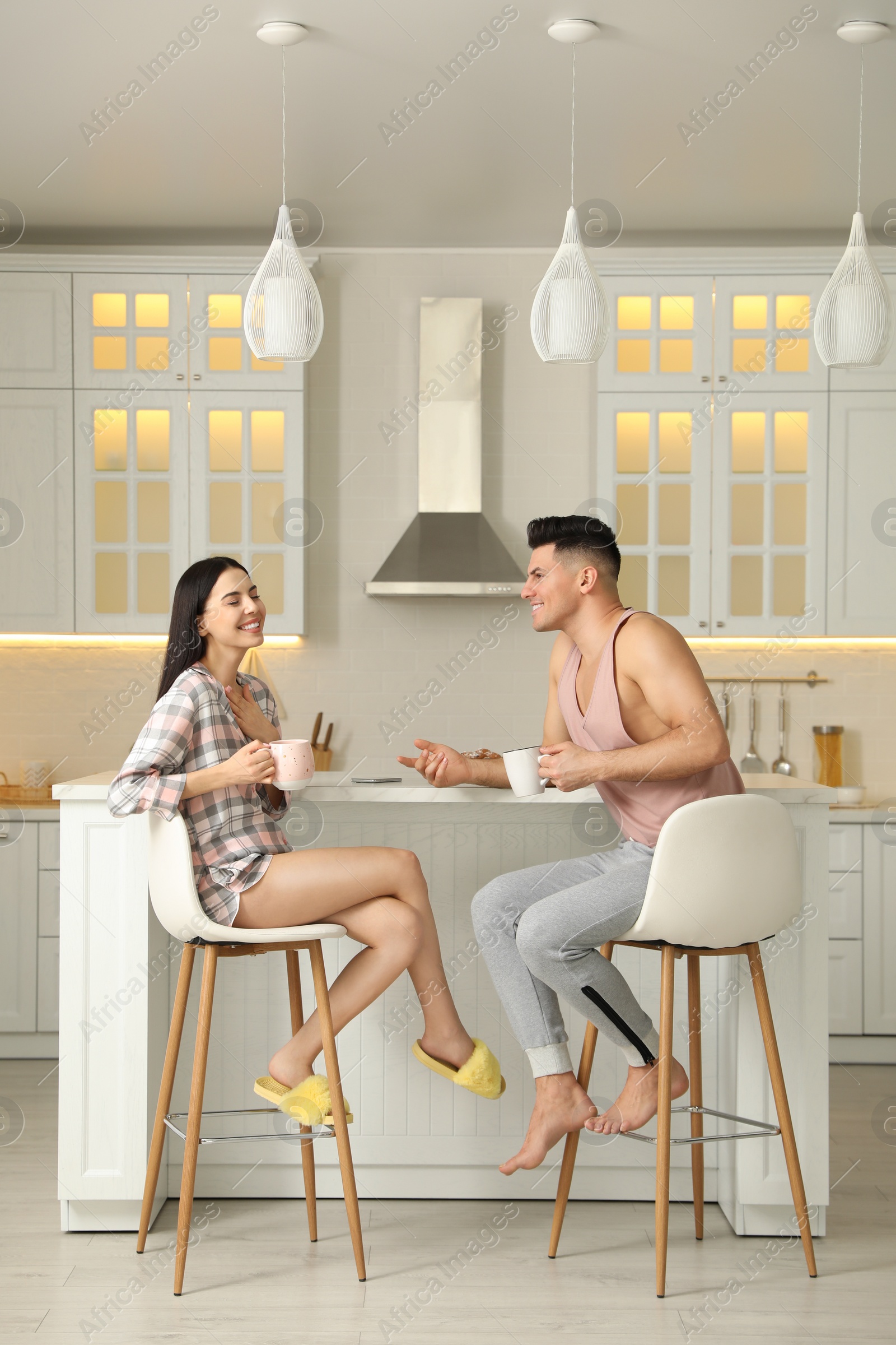 Photo of Happy couple wearing pyjamas during breakfast at table in kitchen