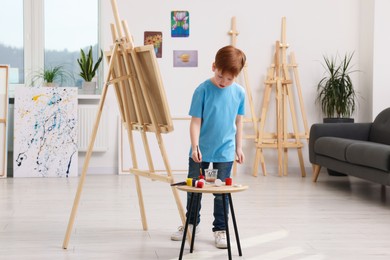 Little boy painting in studio. Using easel to hold canvas