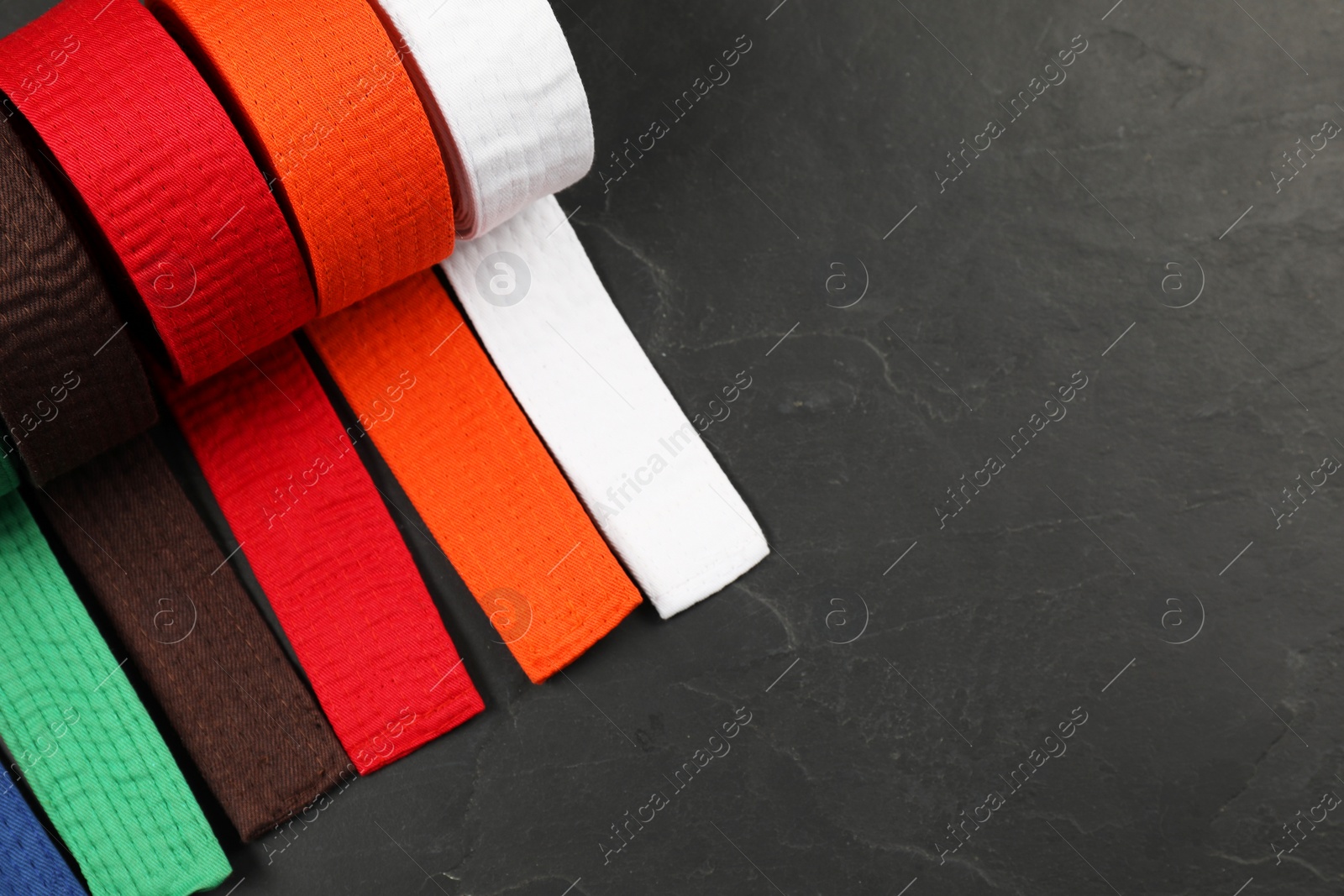 Photo of Colorful karate belts on gray background, flat lay. Space for text