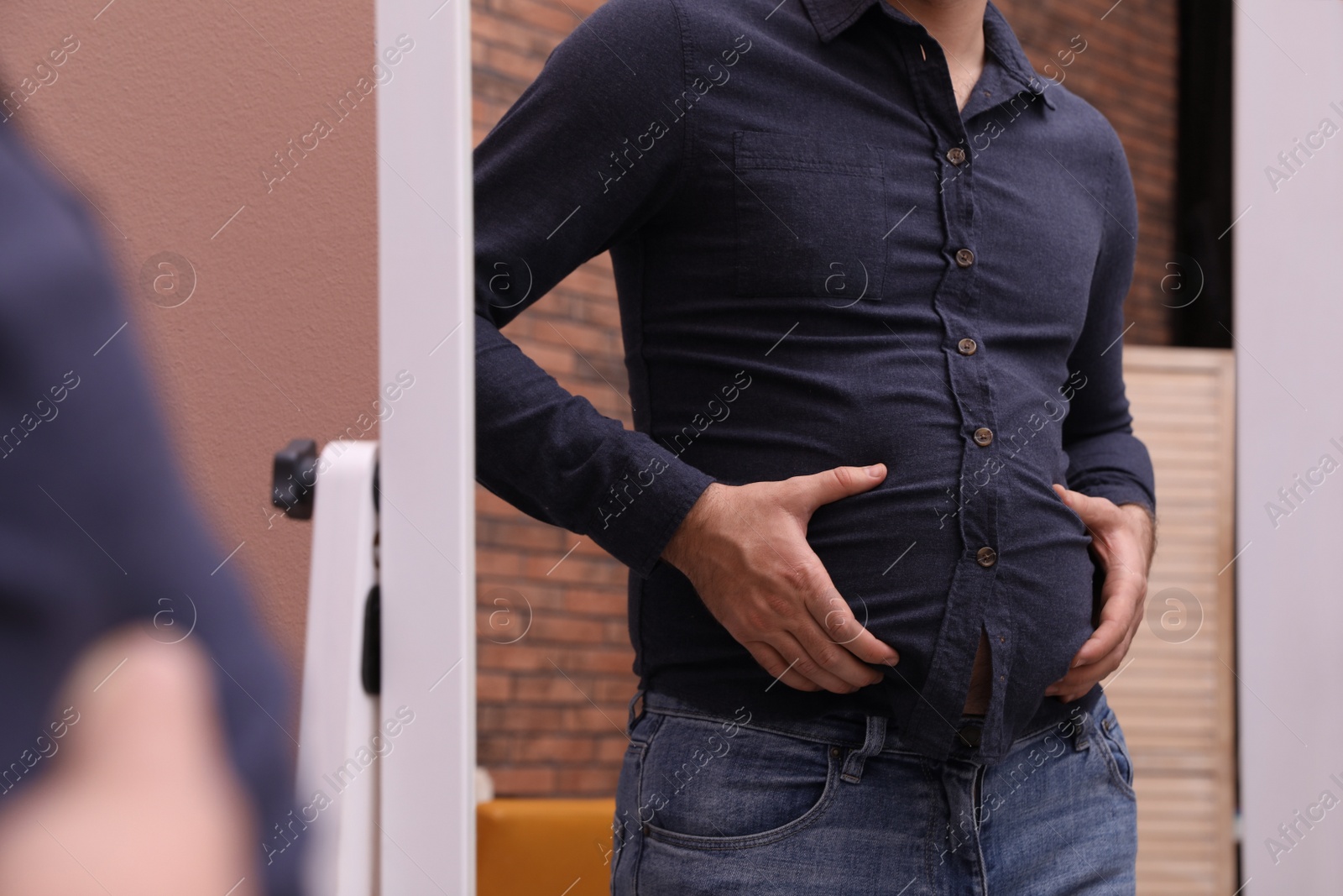 Photo of Man wearing tight shirt in front of mirror indoors, closeup. Overweight problem