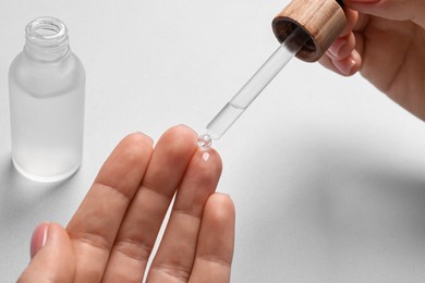 Woman dripping serum from pipette on her hand at white table, closeup