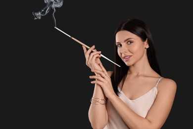 Photo of Woman using long cigarette holder for smoking on black background, space for text