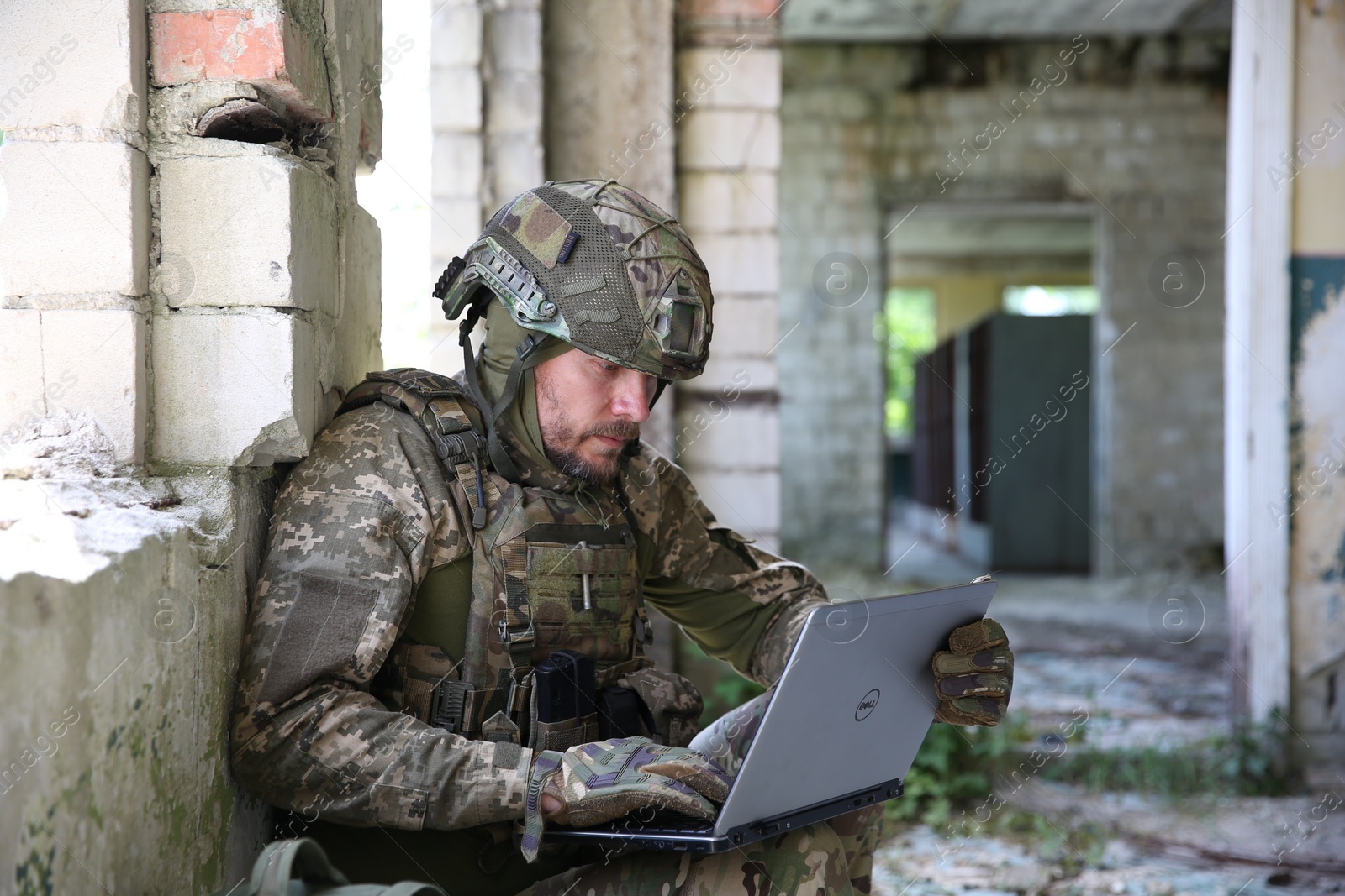 Photo of Military mission. Soldier in uniform using laptop inside abandoned building