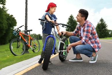 Image of Dad teaching son to ride bicycle outdoors