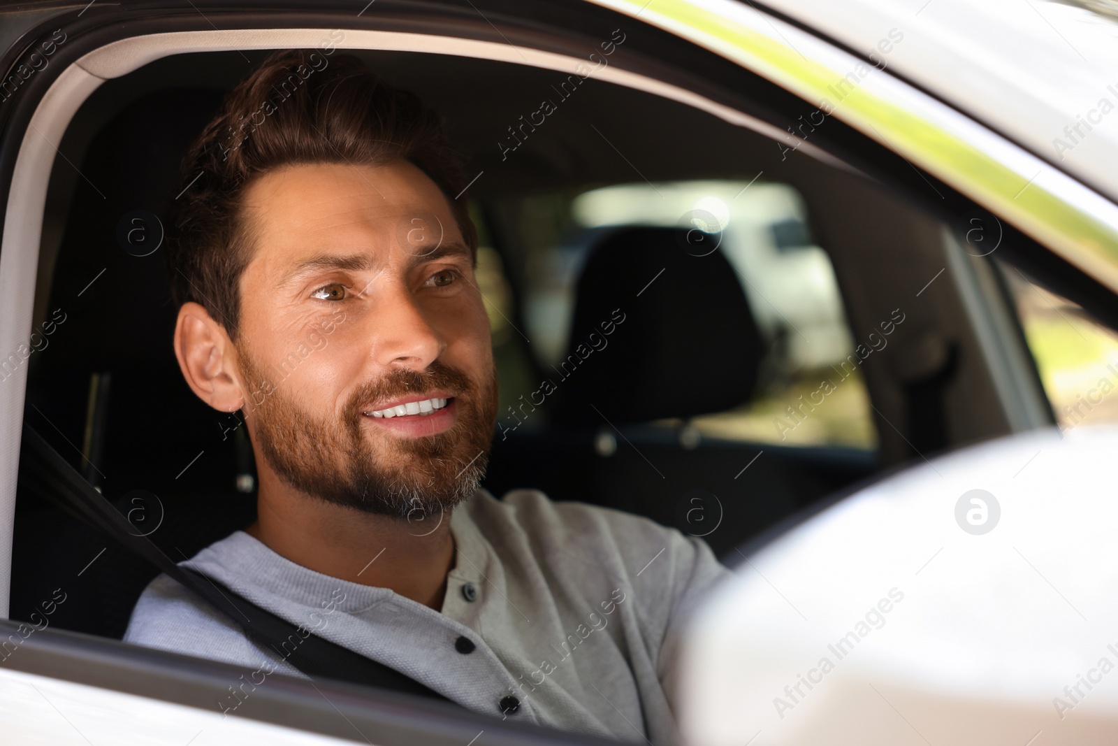 Photo of Happy bearded man sitting in car, view from outside. Enjoying trip