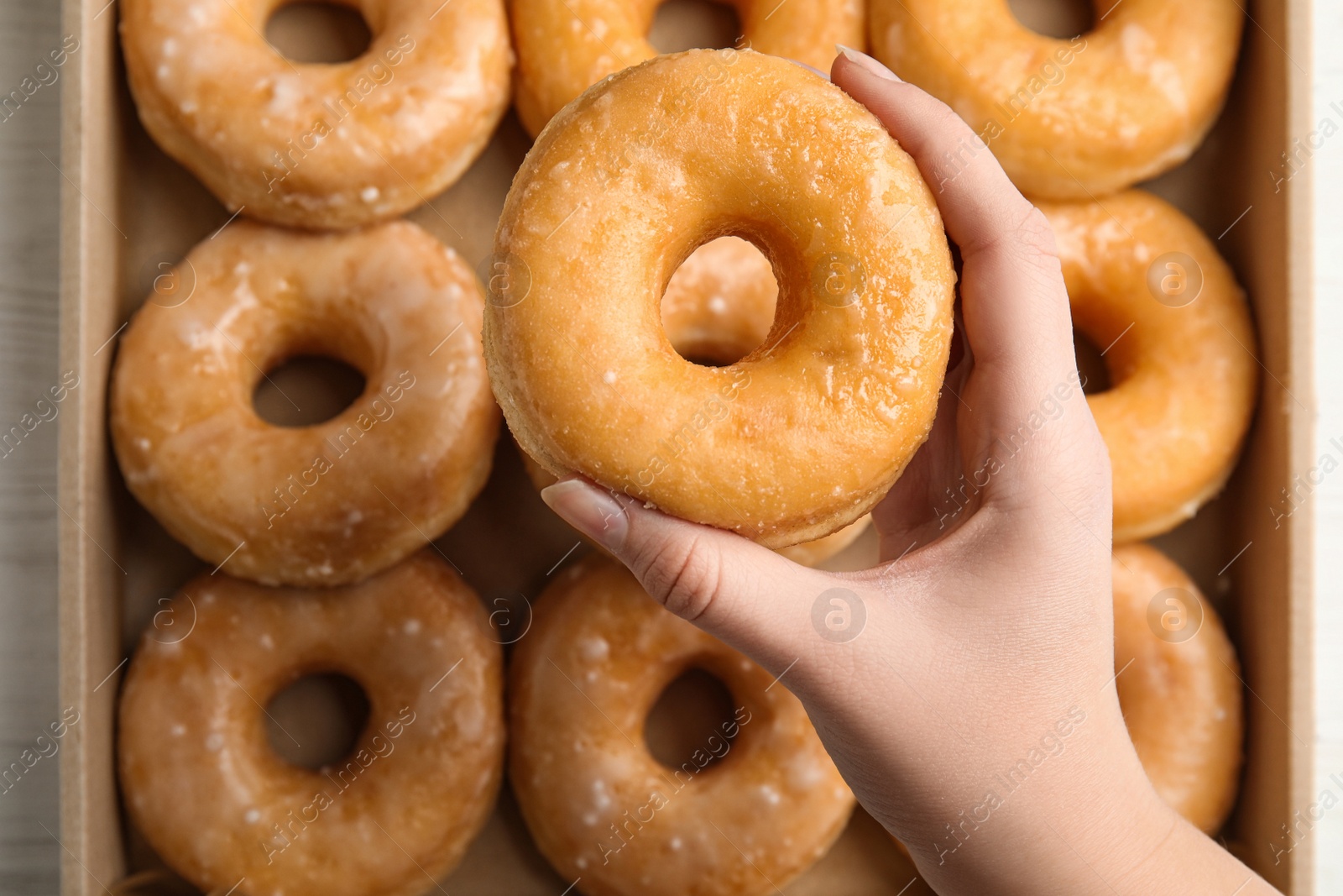 Photo of Woman holding delicious donut at white wooden table, top view