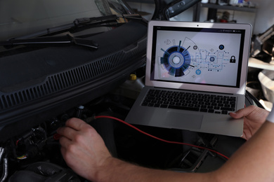 Mechanic with laptop doing car diagnostic at automobile repair shop, closeup