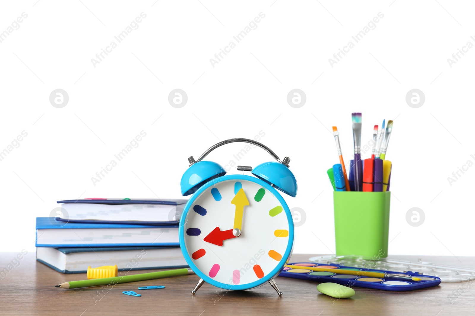 Photo of Light blue alarm clock and different stationery on wooden table against white background. School time