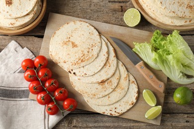 Photo of Tasty homemade tortillas, tomatoes, lime, lettuce and knife on wooden table, top view