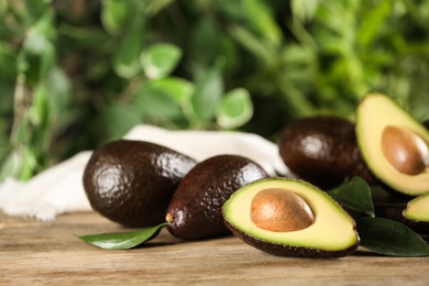 Whole and cut avocados with green leaves on wooden table