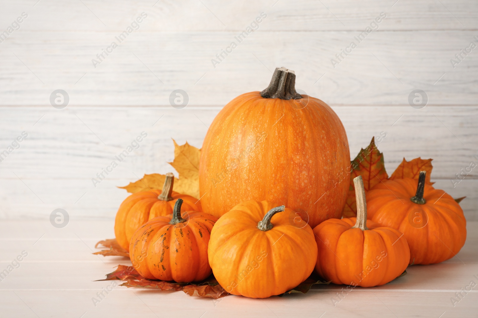 Photo of Pile of ripe pumpkins and dry leaves on white wooden table