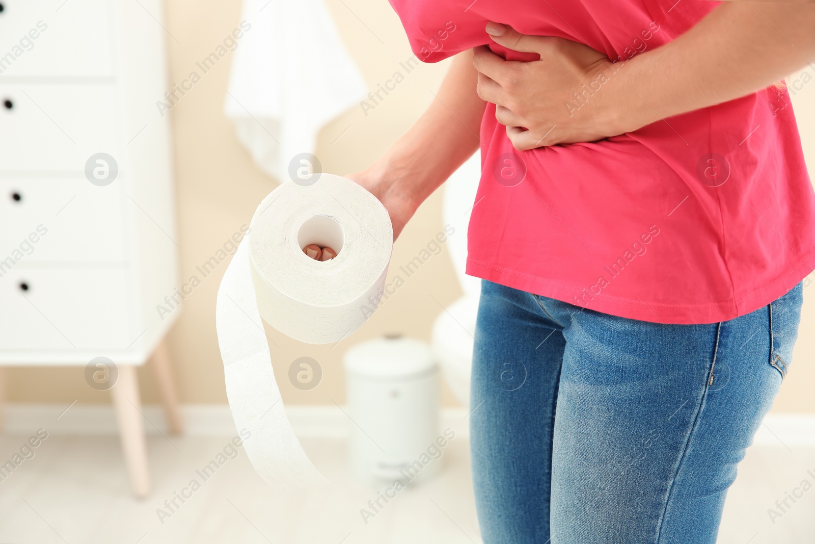 Photo of Young woman with bath tissue standing near toilet bowl at home