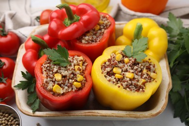 Photo of Quinoa stuffed bell peppers and parsley in baking dish on white table, closeup