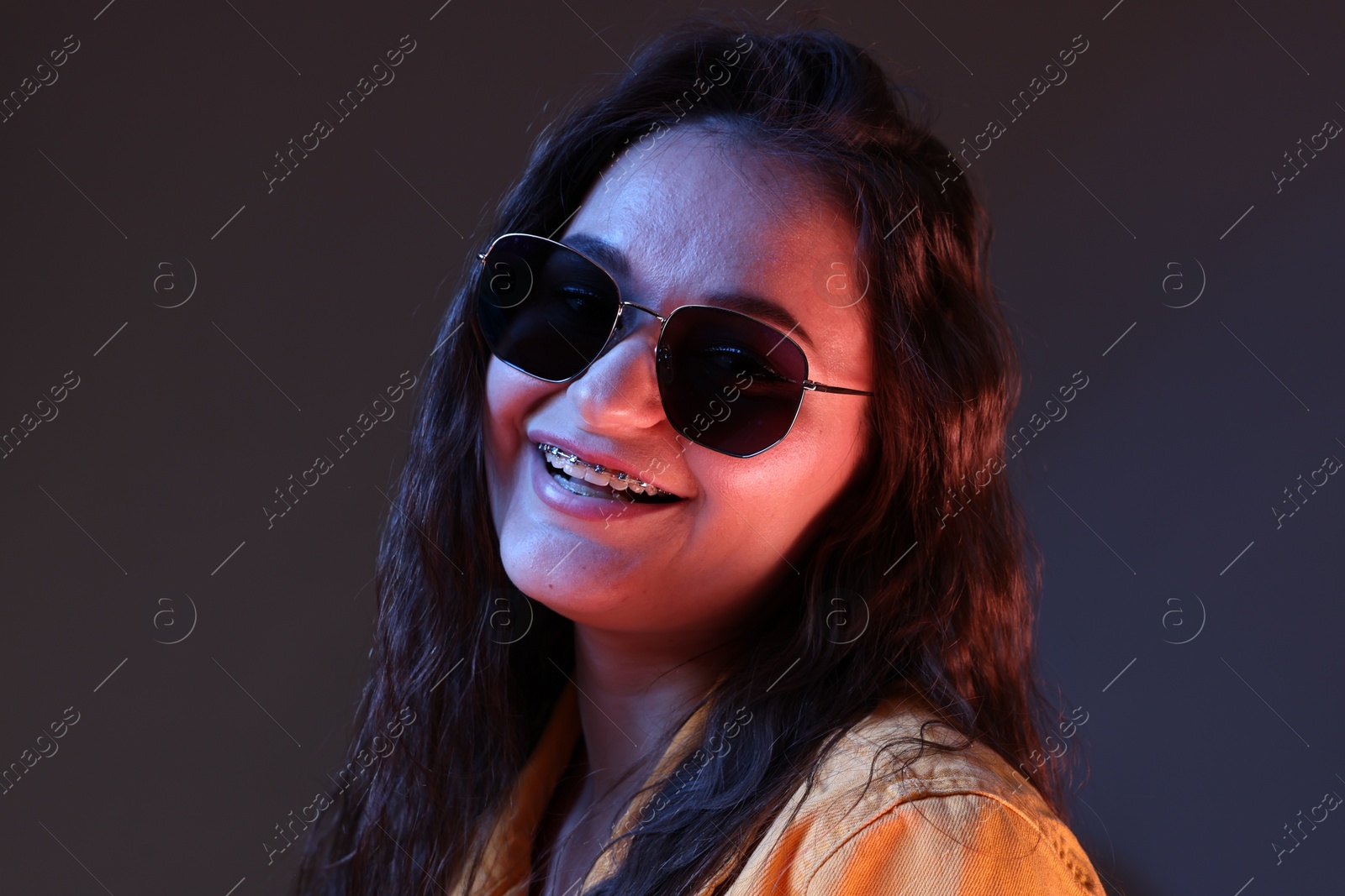 Photo of Portrait of beautiful young woman with stylish sunglasses on color background with neon lights