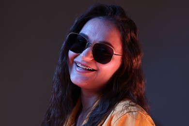 Photo of Portrait of beautiful young woman with stylish sunglasses on color background with neon lights