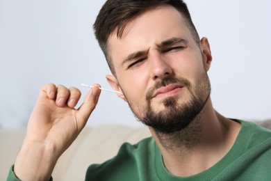 Photo of Young man cleaning ear with cotton swab at home