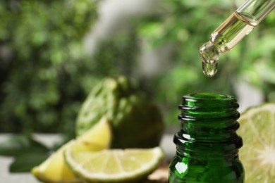 Photo of Dripping bergamot essential oil into glass bottle against blurred background, closeup