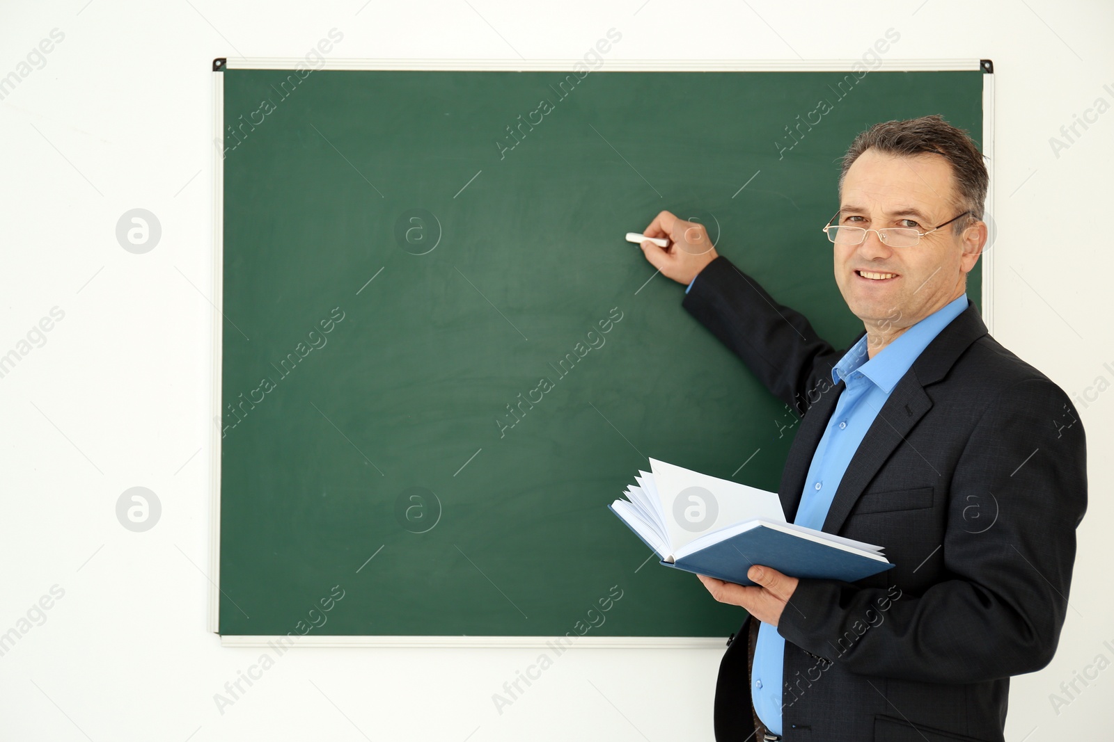 Photo of Male teacher writing on blackboard in classroom