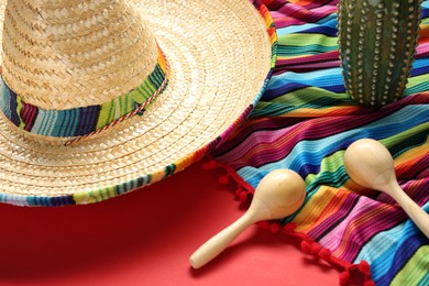 Photo of Mexican sombrero hat, toy cactus, maracas and colorful poncho on red background