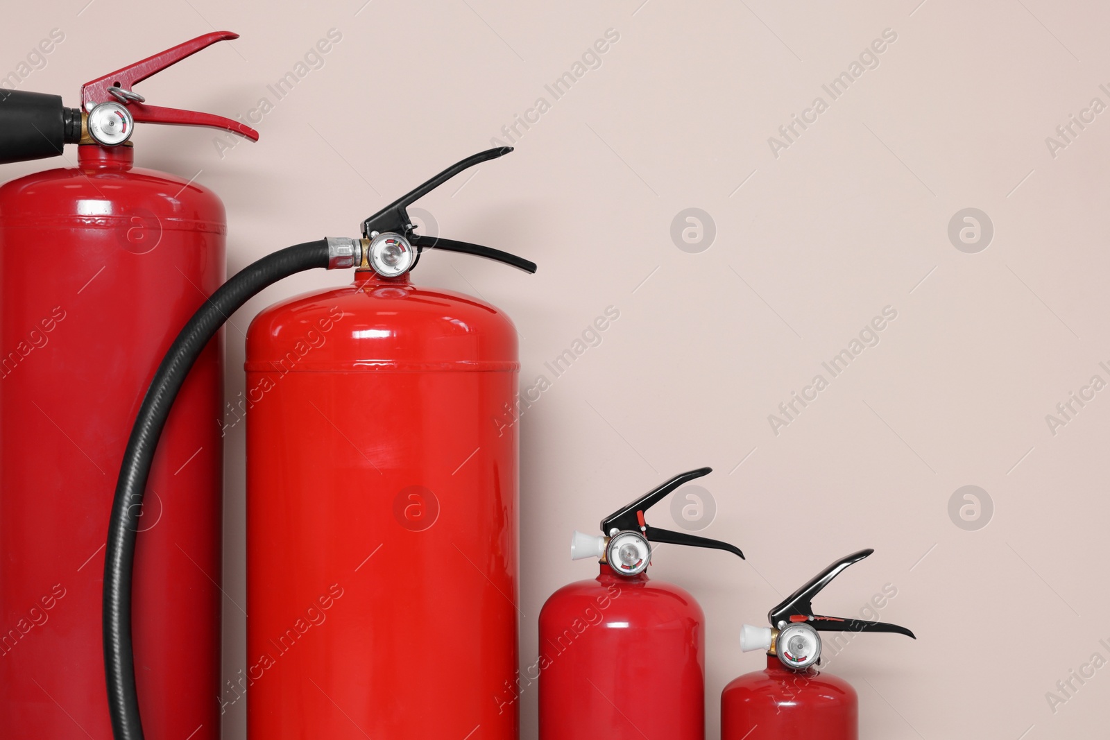 Photo of Set of fire extinguishers on beige background, space for text