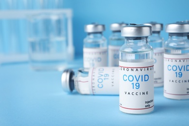 Photo of Vials with coronavirus vaccine on light blue background, space for text