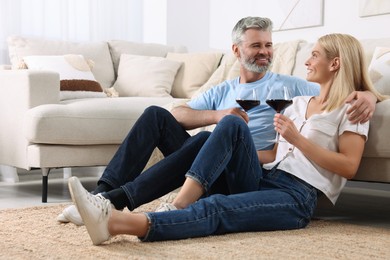 Photo of Happy affectionate couple with glasses of wine on floor at home. Romantic date