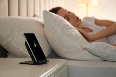 Photo of Smartphone charging on wireless pad and woman sleeping in bed