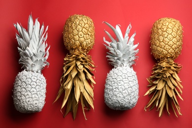 Photo of White and golden pineapples on red background, flat lay. Creative concept