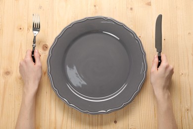 Photo of Woman with fork, knife and empty plate at wooden table, top view