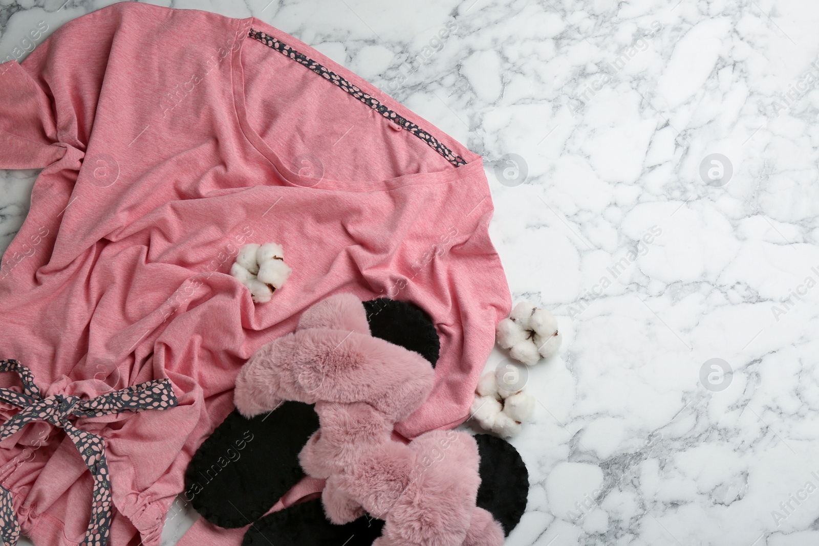 Photo of Pair of fluffy slippers, pajamas and cotton flowers on white marble background, flat lay. Comfortable home outfit