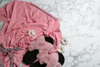 Photo of Pair of fluffy slippers, pajamas and cotton flowers on white marble background, flat lay. Comfortable home outfit