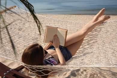 Young woman reading book in hammock on beach