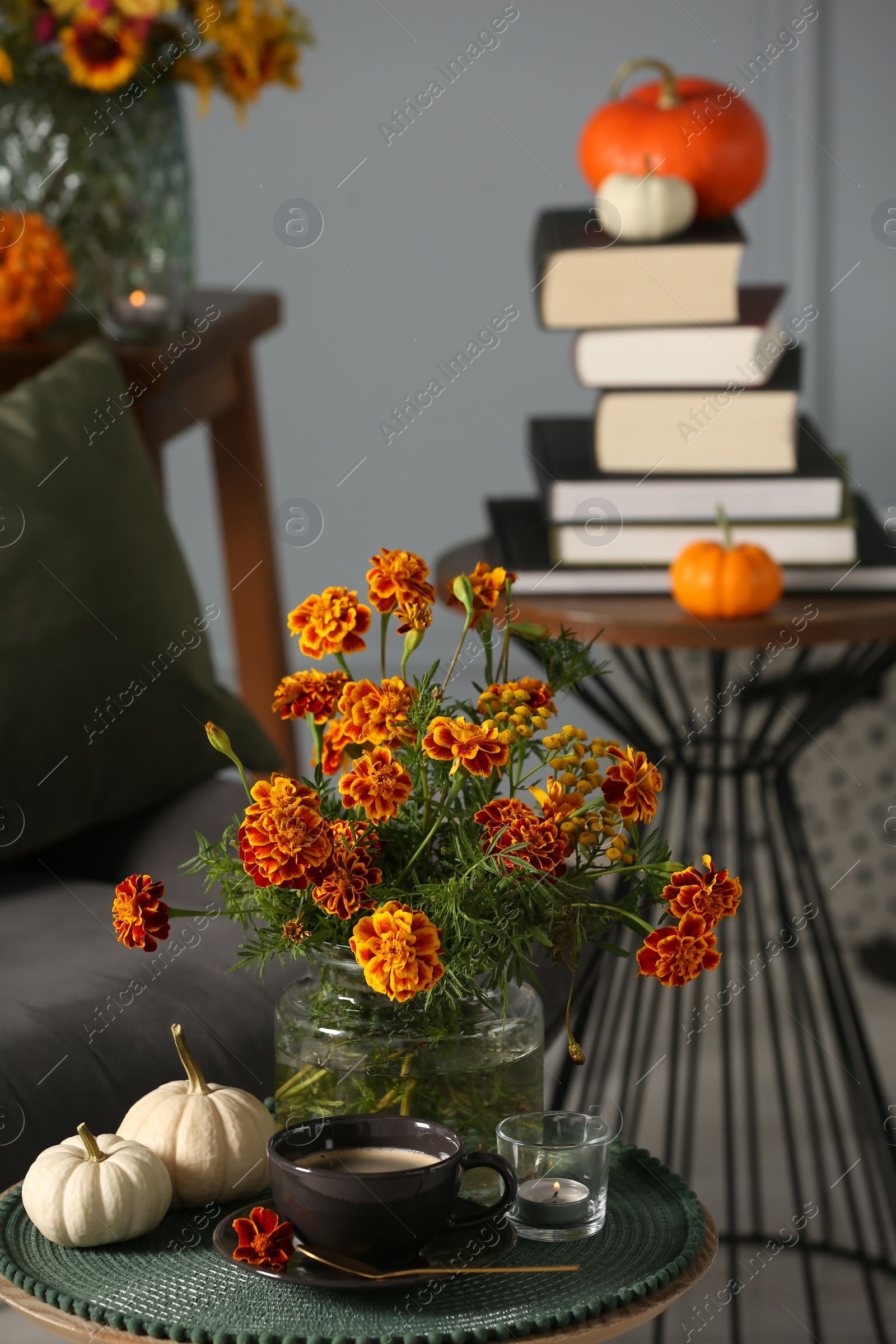 Photo of Beautiful autumn flowers, cup of coffee and pumpkins on side table indoors