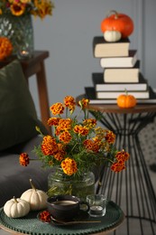 Beautiful autumn flowers, cup of coffee and pumpkins on side table indoors