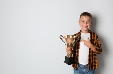 Photo of Happy boy with golden winning cup on light background. Space for text