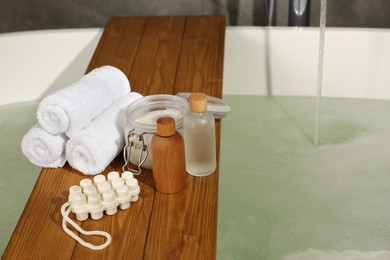 Photo of Wooden tray with spa products and towels on bath tub in bathroom