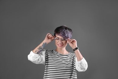 Trendy young woman with tattoo in glasses on color background