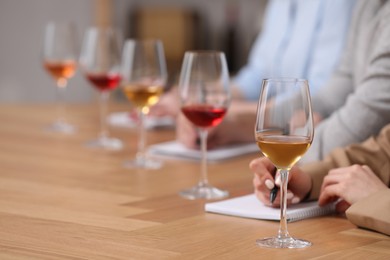 Photo of Sommeliers making notes during wine tasting at table indoors, closeup