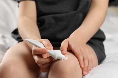 Photo of Child applying ointment onto knee at home, closeup