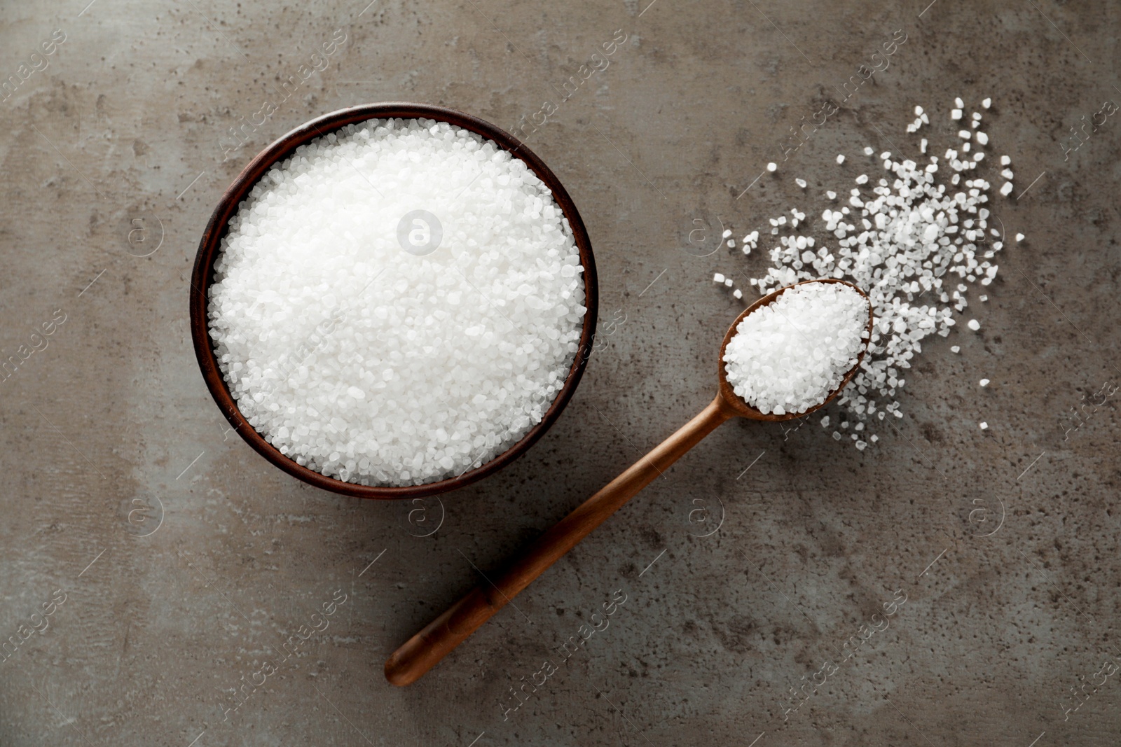 Photo of Bowl and spoon with natural sea salt on grey table, flat lay