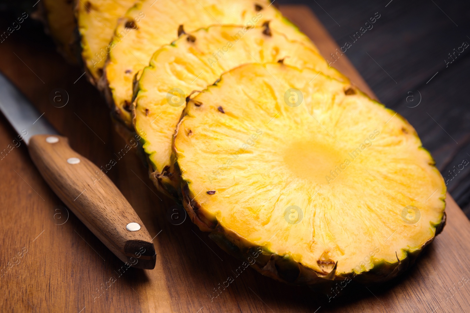 Photo of Tasty cut pineapple and knife on wooden board, closeup