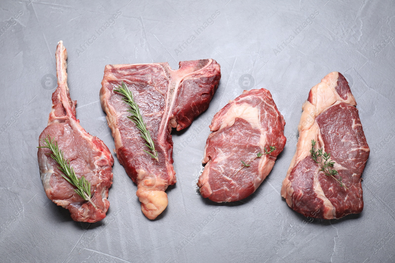 Photo of Fresh raw beef cuts with herbs on light grey textured table, flat lay