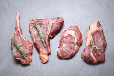 Fresh raw beef cuts with herbs on light grey textured table, flat lay