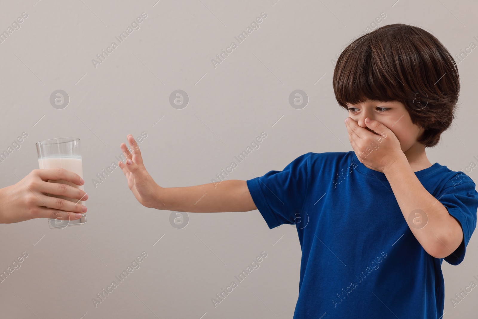 Photo of Cute little boy covering mouth and refusing to drink milk on grey background