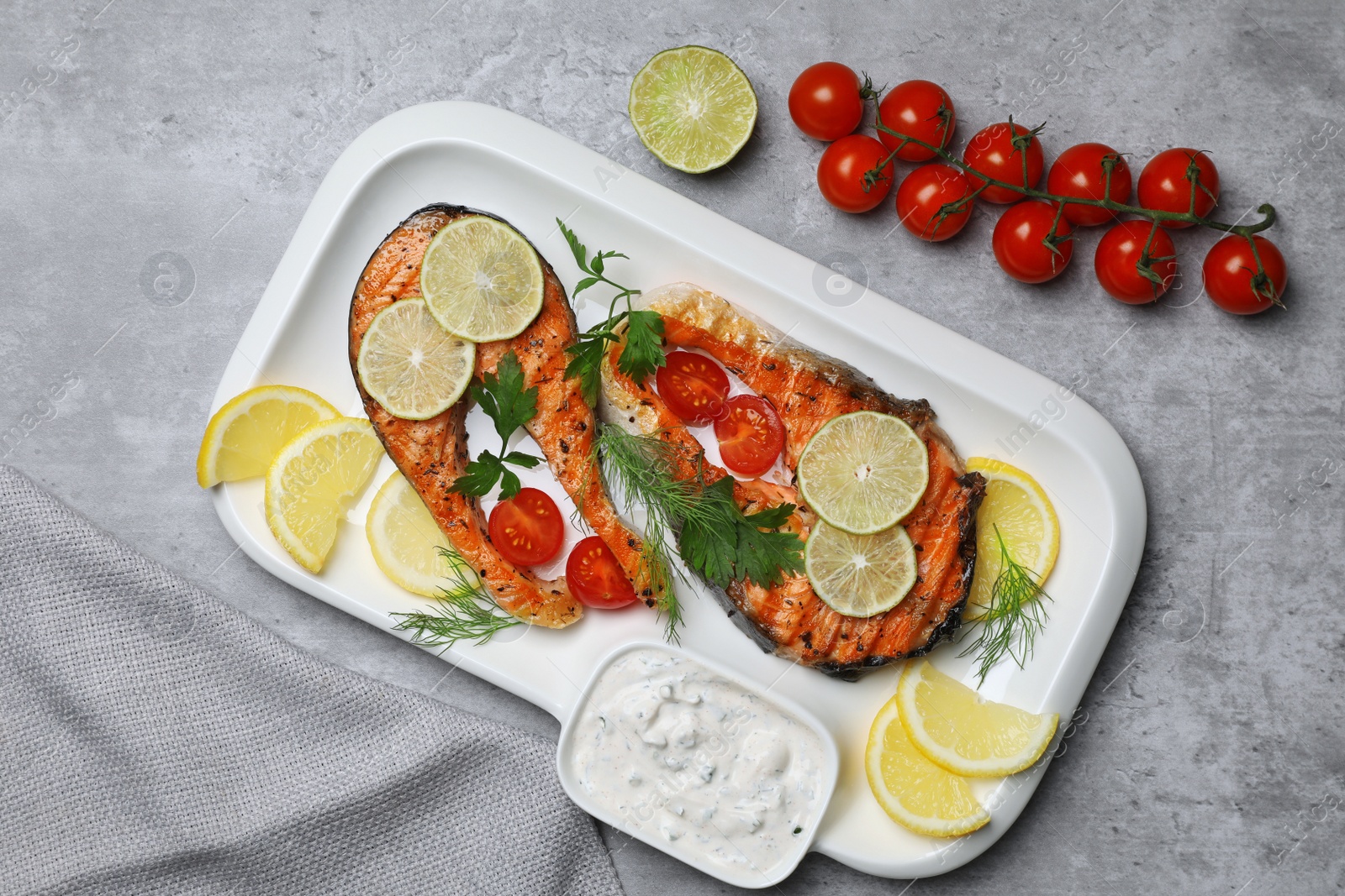 Photo of Tasty grilled salmon steaks and ingredients on light grey table, flat lay