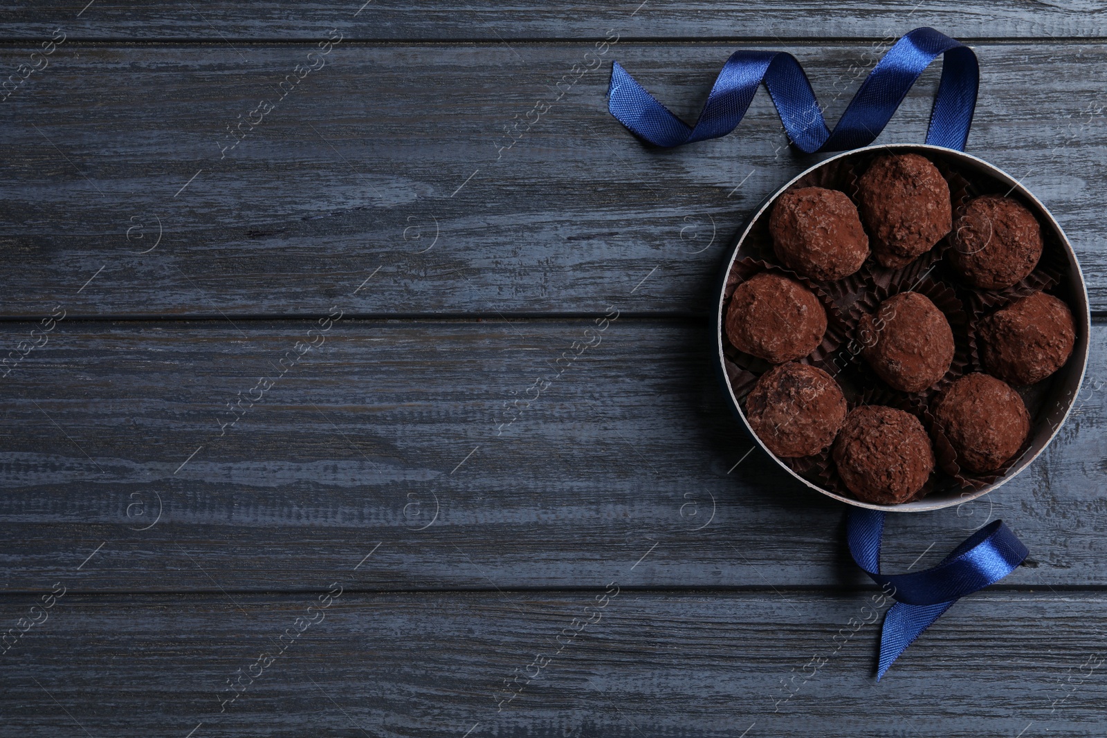 Photo of Box with delicious chocolate truffle candies on dark blue wooden table, flat lay. Space for text