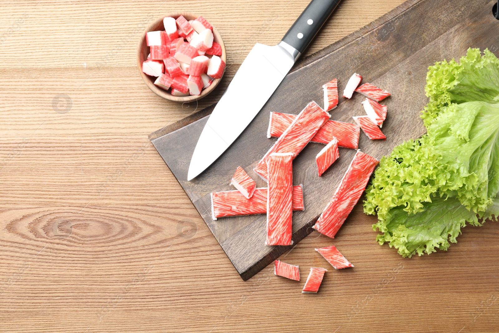 Photo of Delicious crab sticks with lettuce and knife on wooden table, flat lay