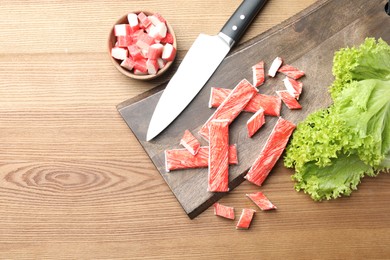 Delicious crab sticks with lettuce and knife on wooden table, flat lay