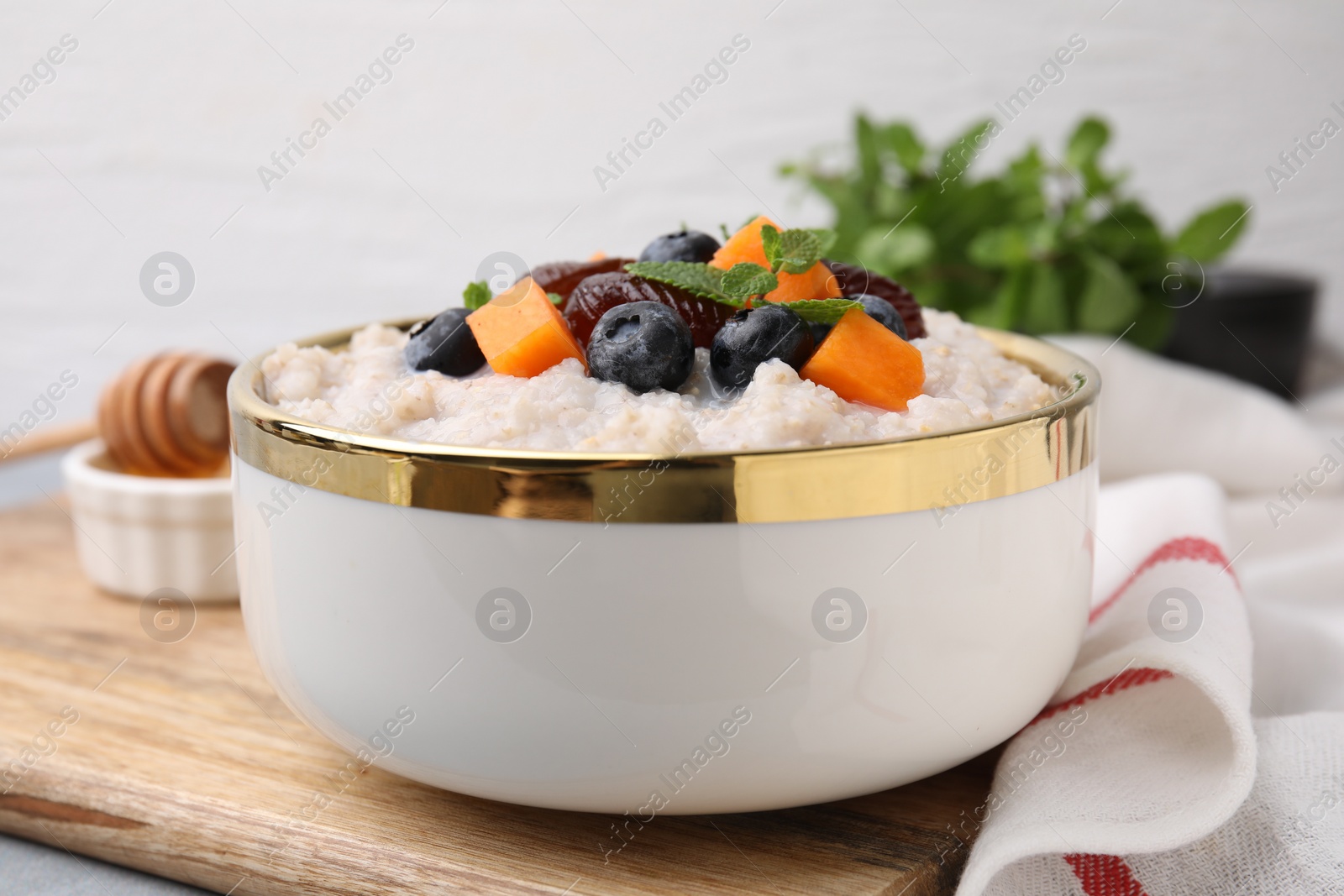 Photo of Delicious barley porridge with blueberries, pumpkin, dates and mint in bowl on table, closeup