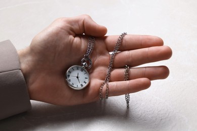 Photo of Man holding chain with elegant pocket watch at light textured table, closeup